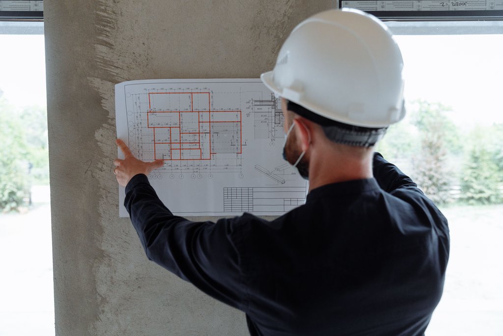 Architekt mit Bauhelm betrachtet einen Grundriss auf der Baustelle